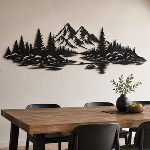 Op de afbeelding: Een wanddecoratie van zwart metaal met een gedetailleerd landschapssilhouet van grillige bergtoppen, een dicht dennenbos en een kalm meer met rotsachtige oevers. Het ontwerp is langwerpig en horizontaal met ingewikkelde uitsparingen.