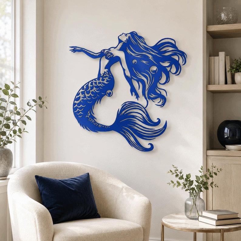 Puede incluir: Una pieza de arte mural de metal azul con forma de sirena, con cabello largo y fluido y una cola detallada. La silueta presenta secciones recortadas que definen los mechones de cabello y las escamas, creando una pose din&aacute;mica hacia arriba.
