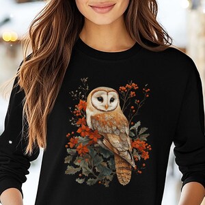 May include: A black long-sleeved sweatshirt with a white barn owl and autumn leaves graphic. The owl is perched on a branch with red berries and green leaves. The text "Bella Canvas 3501 Black" is visible in the lower left corner of the image.