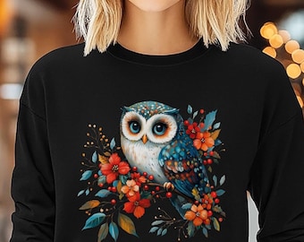May include: A black cropped sweatshirt with a colorful owl and floral design. The owl has blue and white feathers and large, round eyes. The flowers are red, orange, and yellow.