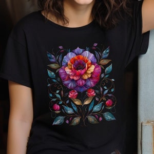 May include: Black t-shirt with a colorful floral design. The design features a large flower with pink, purple, red, and orange petals, surrounded by green leaves and vines.