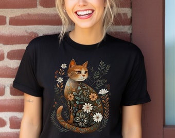 May include: A black t-shirt with a graphic of an orange cat surrounded by flowers. The cat is sitting with its tail curled around its body.