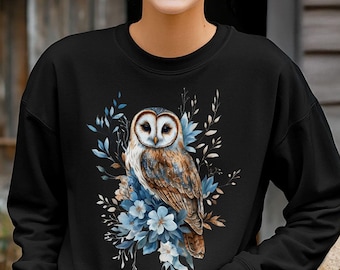 May include: Black sweatshirt with a graphic print of an owl with blue flowers and leaves. The text "Bella Canvas 3501 Black" is printed on the bottom left corner of the image.