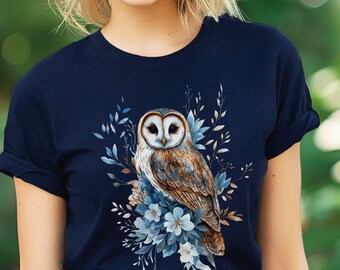 May include: A navy blue t-shirt with a white and blue floral design featuring an owl. The owl is brown and white with yellow eyes. The text "Bella Canvas Navy" is visible in the lower right corner of the image.