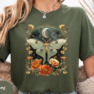 May include: A green t-shirt with a graphic of a moon, a moth, and flowers. The text "Bella Canvas Military Green" is at the bottom of the image.
