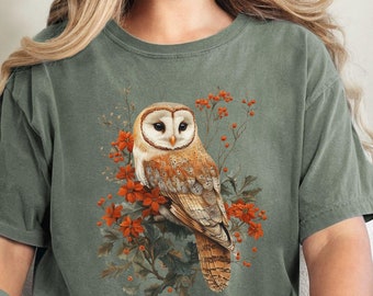 May include: A green t-shirt with a white barn owl with orange flowers and berries on a branch. The text "Comfort Colors Moss" is in the bottom left corner of the image.
