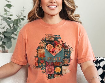 May include: A terracotta colored t-shirt with a graphic of a patchwork heart with the word "Peace" inside. The heart is surrounded by flowers and other designs.