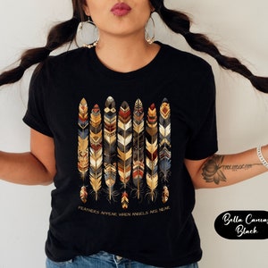 May include: Black t-shirt with a design of colorful feathers and the text "Feathers appear when angels are near".