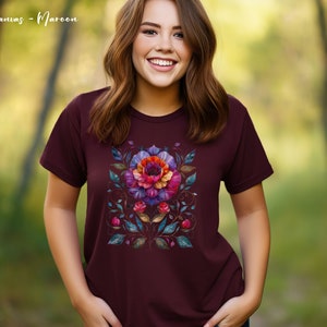 May include: A maroon t-shirt with a colorful floral design. The design features a large flower with pink, purple, and orange petals, surrounded by smaller flowers and leaves in shades of blue, green, and gold.