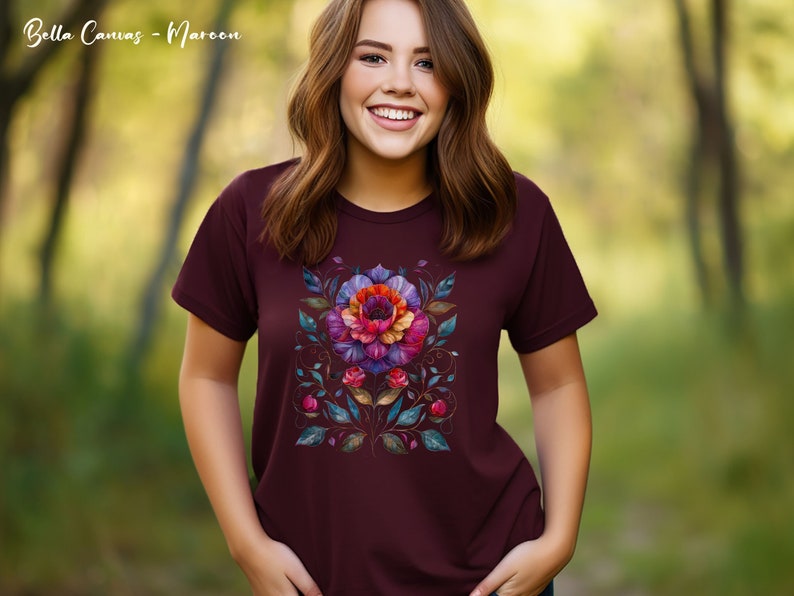 May include: A maroon t-shirt with a colorful floral design. The design features a large flower with pink, purple, and orange petals, surrounded by smaller flowers and leaves in shades of blue, green, and gold.