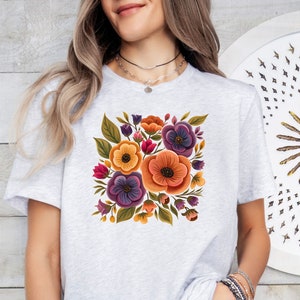 May include: A white t-shirt with a floral design featuring purple, orange, yellow, and green flowers. The flowers are arranged in a bouquet shape.