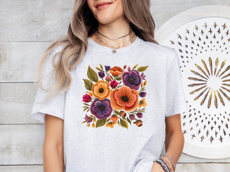 May include: A white t-shirt with a floral design featuring purple, orange, yellow, and green flowers. The flowers are arranged in a bouquet shape.