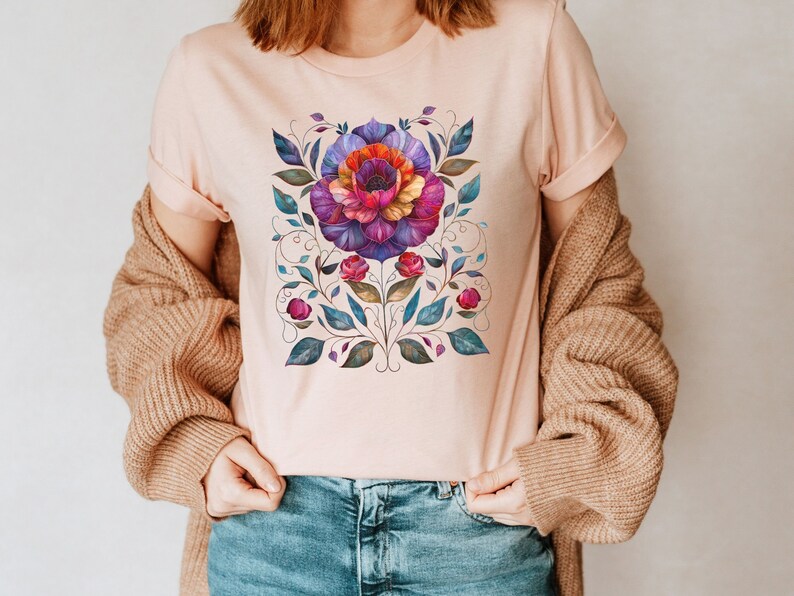 May include: A pink t-shirt with a colorful floral design. The design features a large flower with pink, purple, and orange petals, surrounded by green leaves and vines.