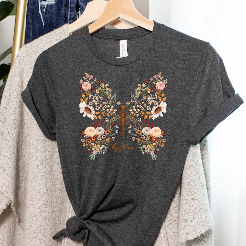May include: A dark gray t-shirt with a floral butterfly design and the text "Be Free" printed on the front.
