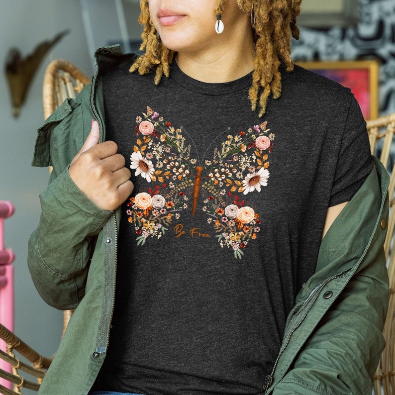May include: A dark heather grey t-shirt with a floral butterfly design and the text "Be Free".