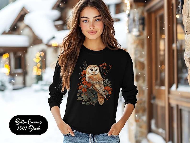 May include: A black long-sleeved sweatshirt with a white barn owl and autumn leaves graphic. The owl is perched on a branch with red berries and green leaves. The text "Bella Canvas 3501 Black" is visible in the lower left corner of the image.