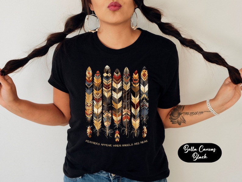 May include: Black t-shirt with a design of colorful feathers and the text "Feathers appear when angels are near".