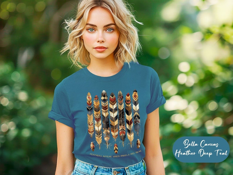 May include: A teal blue t-shirt with a graphic of colorful feathers and the text "FEATHERS APPEAR WHEN ANGELS ARE NEAR". Bella Canvas Heather Deep Teal.