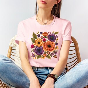 May include: A pink t-shirt with a floral print featuring orange, yellow, purple, and green flowers.