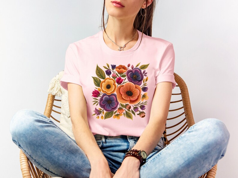 May include: A pink t-shirt with a floral print featuring orange, yellow, purple, and green flowers.