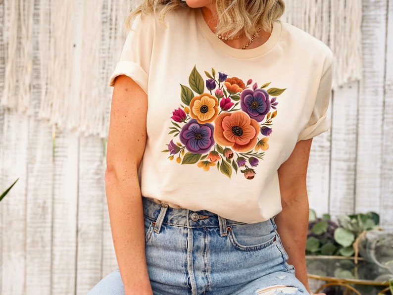 May include: A cream colored t-shirt with a floral print featuring purple, orange, yellow, and green flowers.