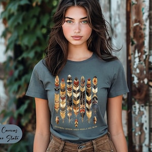 May include: A heather slate gray t-shirt with a graphic of stylized feathers in shades of brown, gold, and red. The text "FEATHERS APPEAR WHEN ANGELS ARE NEAR" is printed below the graphic.