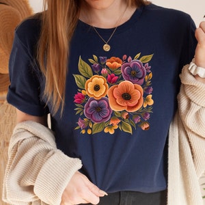 May include: A navy blue t-shirt with a floral print featuring yellow, orange, purple, and pink flowers. The flowers are arranged in a square shape and have a vintage style.