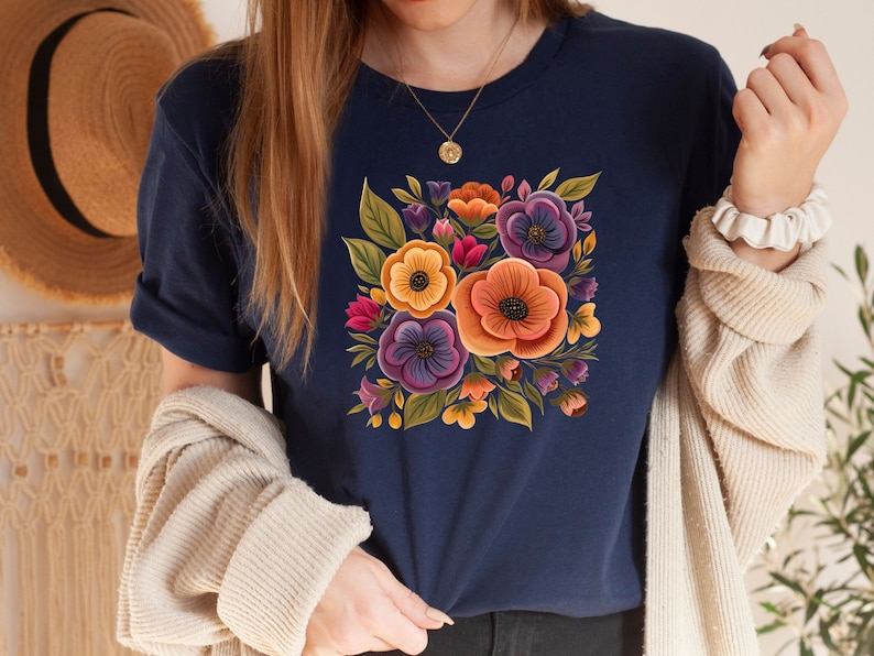May include: A navy blue t-shirt with a floral print featuring yellow, orange, purple, and pink flowers. The flowers are arranged in a square shape and have a vintage style.
