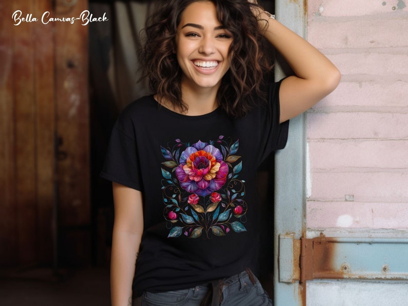 May include: Black t-shirt with a colorful floral design. The design features a large flower with pink, purple, red, and orange petals, surrounded by green leaves and vines.