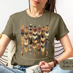 May include: A green t-shirt with a design of colorful feathers and the text "Feathers appear when angels are near".