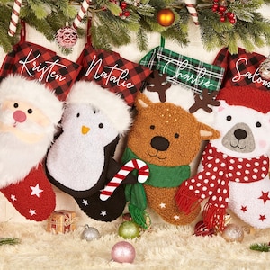 Peut inclure: Quatre chaussettes de Noël personnalisées avec différents personnages d'animaux. Les chaussettes sont en tissu à carreaux rouge et noir, vert et blanc, blanc à pois rouges et blanc à étoiles rouges. Les chaussettes sont décorées d'un Père Noël, d'un pingouin, d'un renne et d'un ours polaire.