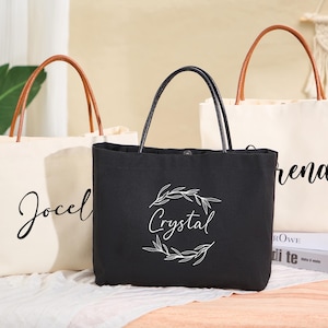 May include: Three tote bags with personalized names. The bags are made of canvas and have brown leather handles. The names on the bags are "Jocelyn", "Crystal", and "Brenda".