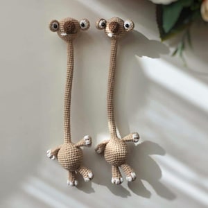 Pode incluir: Duas bonecas alienígenas feitas à mão em crochê. As bonecas têm pescoços longos, corpos pequenos e braços e pernas minúsculos. As cabeças têm olhos grandes e pequenos sorrisos. As bonecas são bege com detalhes brancos.