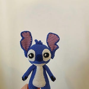 May include: A handmade blue and white crochet Stitch doll with large ears and black eyes. The doll has a white belly and black feet. The doll is approximately 4 inches tall.
