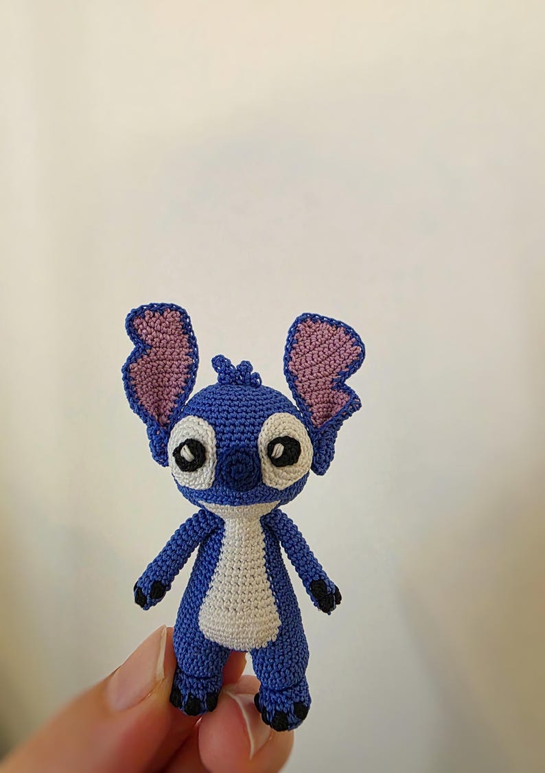 May include: A handmade blue and white crochet Stitch doll with large ears and black eyes. The doll has a white belly and black feet. The doll is approximately 4 inches tall.