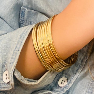 May include: A stack of gold bangles with a hammered finish. The bangles are worn on a person's wrist.