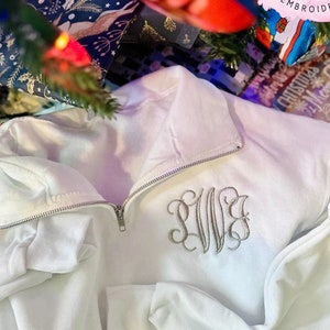 May include: White zippered sweatshirt with a monogrammed "LWS" embroidered on the front. The sweatshirt is laying on a wood surface.