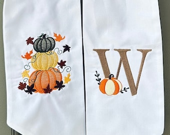 May include: White door swag with a stack of pumpkins and fall leaves on one side and the letter "W" with a small pumpkin on the other side.