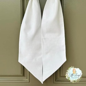 May include: A white fabric bow with a pointed end, tied around a green wreath. The bow is hanging on a green door.