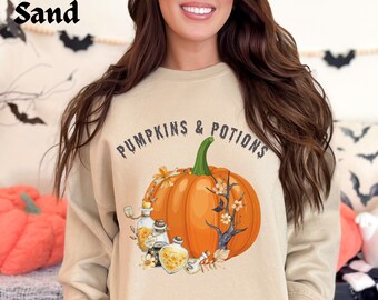 May include: Sand-colored sweatshirt with the text "PUMPKINS & POTIONS" above a graphic of an orange pumpkin, potion bottles, and floral accents. The sweatshirt is a neutral color, perfect for fall and Halloween.