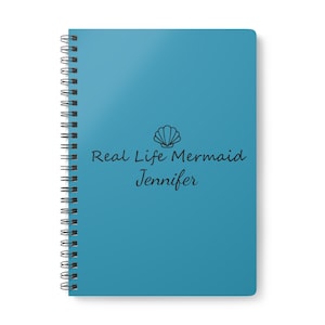 May include: A teal spiral-bound notebook with the text "Real Life Mermaid Jennifer" and a seashell graphic. The notebook has a glossy cover and a silver spiral binding.