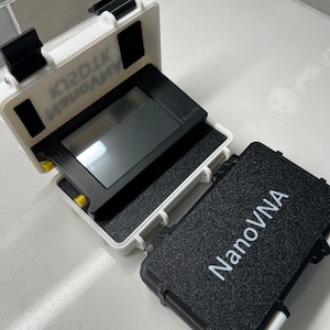 May include: A white hard case with a black NanoVNA device inside. The case has a black foam interior and a black latch. The device has a black screen and a white label that says "NanoVNA".