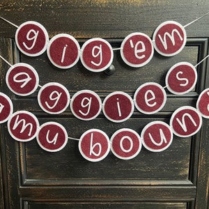 May include: A maroon felt banner with white letters spelling "Gig 'em Aggies Bound".