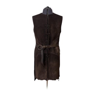 May include: A dark brown sleeveless tunic made of suede leather, featuring a vertical lace-up closure down the centre back and a matching leather belt secured with a circular metal ring at the waist, displayed on a mannequin torso.