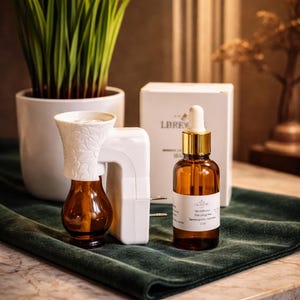 May include: A white plug-in oil diffuser with a floral embossed top and an amber glass bottle, accompanied by a matching amber glass dropper bottle labeled LBREW Sampaguita-Jasmine 2 oz, positioned in front of a white product box.