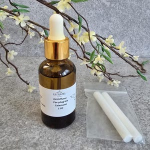 May include: A brown glass bottle with a gold lid and a white dropper top. The bottle is labeled "Lil Hazel" and contains an oil diffuser for plug-ins. The label also states "Calamansi" and "1 oz". Two white reeds are included in a clear plastic bag.