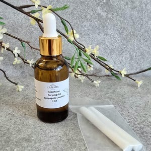 May include: A brown glass bottle with a gold lid and a white dropper top. The bottle is labeled "Lil Hazel Oil Diffuser for plug-ins Sampaguita-Jasmine 1 OZ". The bottle is next to a clear plastic bag containing two white reed diffusers.