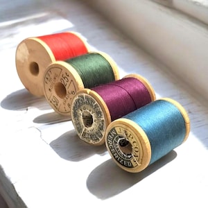 Può includere: Quattro bobine di filo con rocchetti di legno. Le bobine sono rosse, verdi, viola e blu. I rocchetti sono etichettati con testo che include "Fast Boiling", "Shade 225", "J & P Coats" e "Mercerized".