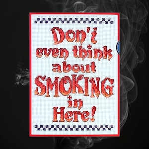 Puede incluir: Un cartel blanco de punto de cruz con texto rojo y naranja que dice "No pienses ni por un momento en FUMAR aquí!" El cartel tiene un borde a cuadros blanco y negro.