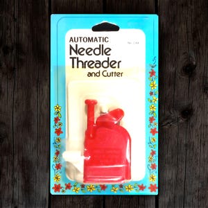 May include: A red automatic needle threader and cutter in its original packaging. The package is light blue with floral accents and the text "AUTOMATIC Needle Threader and Cutter".